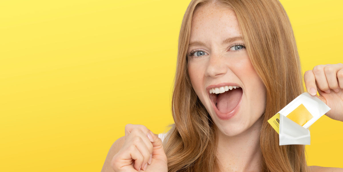 Woman holding an open RIN Glow Strip sachet with a yellow tongue strip visible against a bright yellow background.