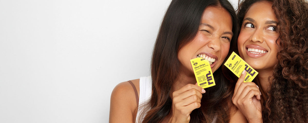 Two women holding yellow RIN Glow Strips sachets and smiling against a white background.