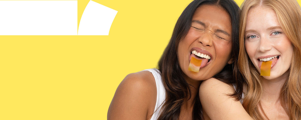 Two women with RIN tongue strips on their tongues posing against a bright yellow background.